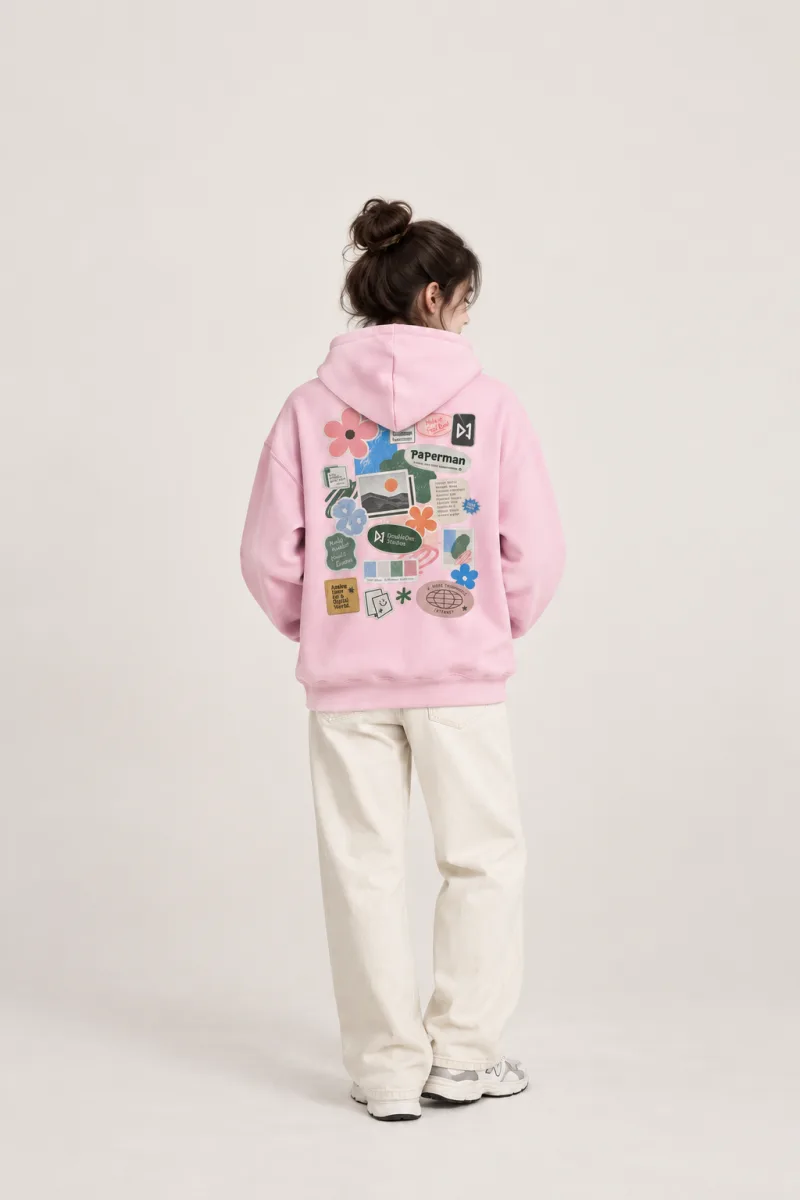Model wearing the pink Paperman hoodie, with a sticker-collage print on the back